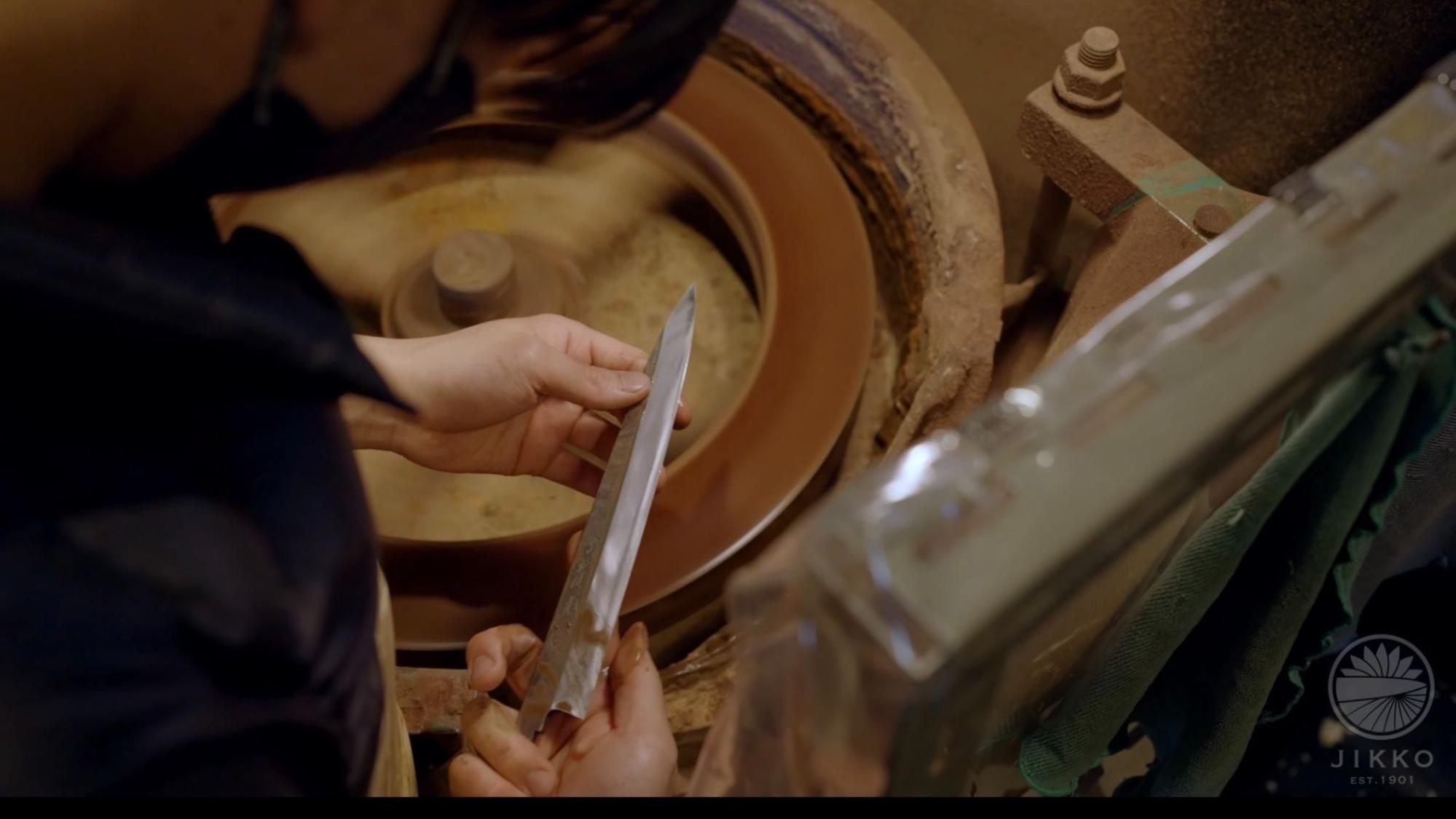 大阪・堺の實光刃物の工房で、職人が包丁を使いながら研ぎ直しについて説明している様子